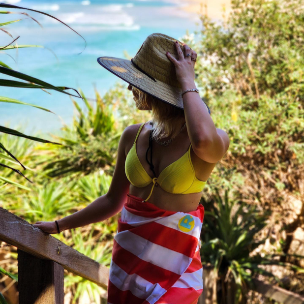 Girl wearing a hat and a Rockycay red sand free beach towel at the beach