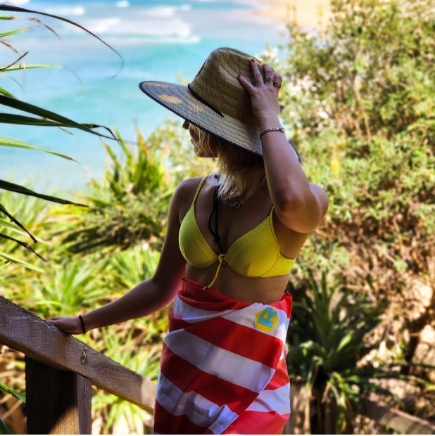 Girl wearing a hat and a Rockycay red sand free beach towel at the beach 