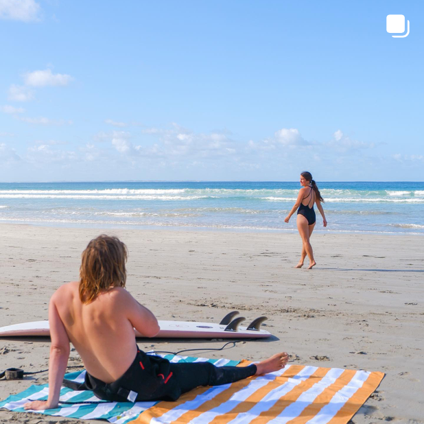 Surfer sitting on a couple of quick drying beach towels at the beach