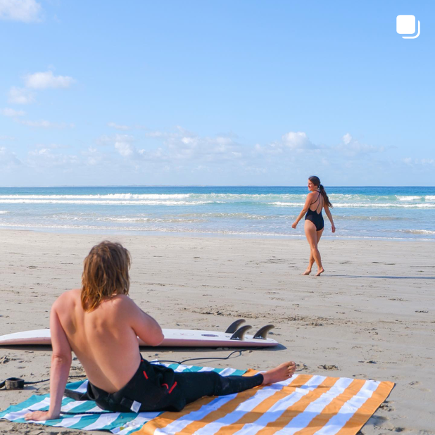 Surfer sitting on a couple of quick drying beach towels at the beach 