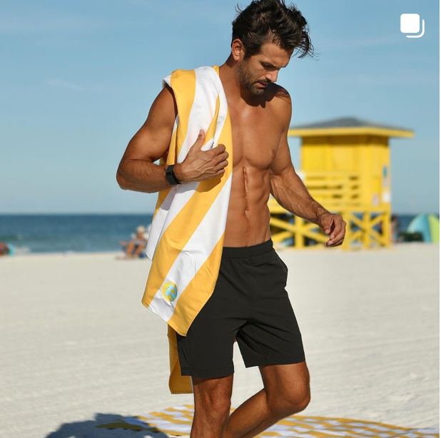 Man walking with an orange striped beach towel on the sand